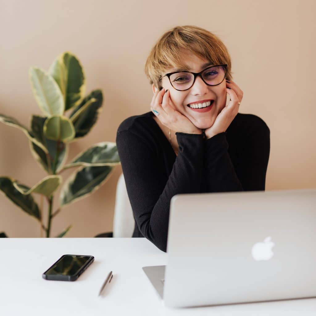 Woman smiling at the camera in front of an open laptop, illustrating happiness about her caring accounting